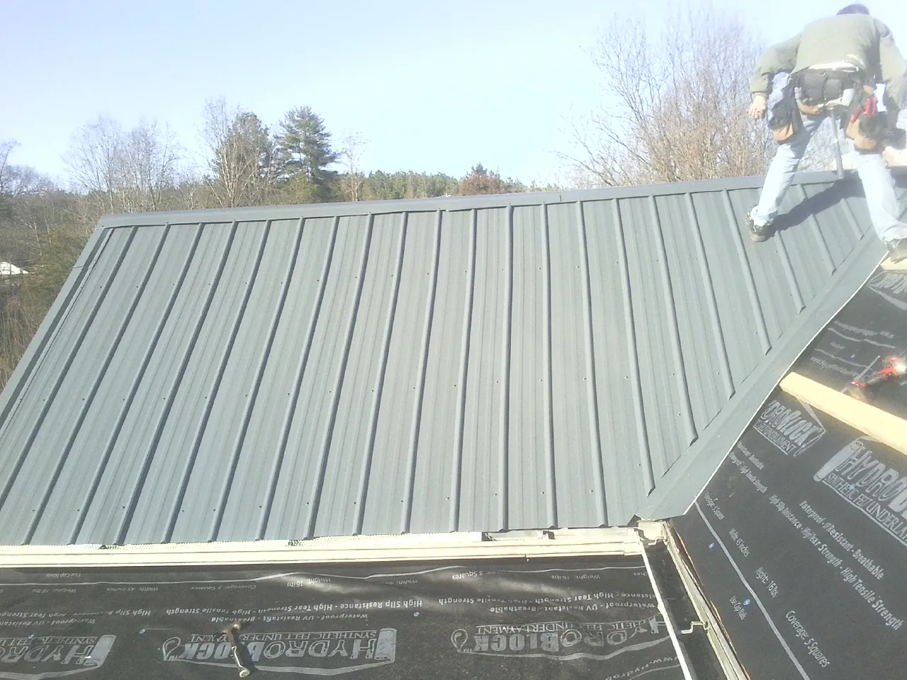 Crew installing dark green standing seam panels over synthetic underlayment in Richlands