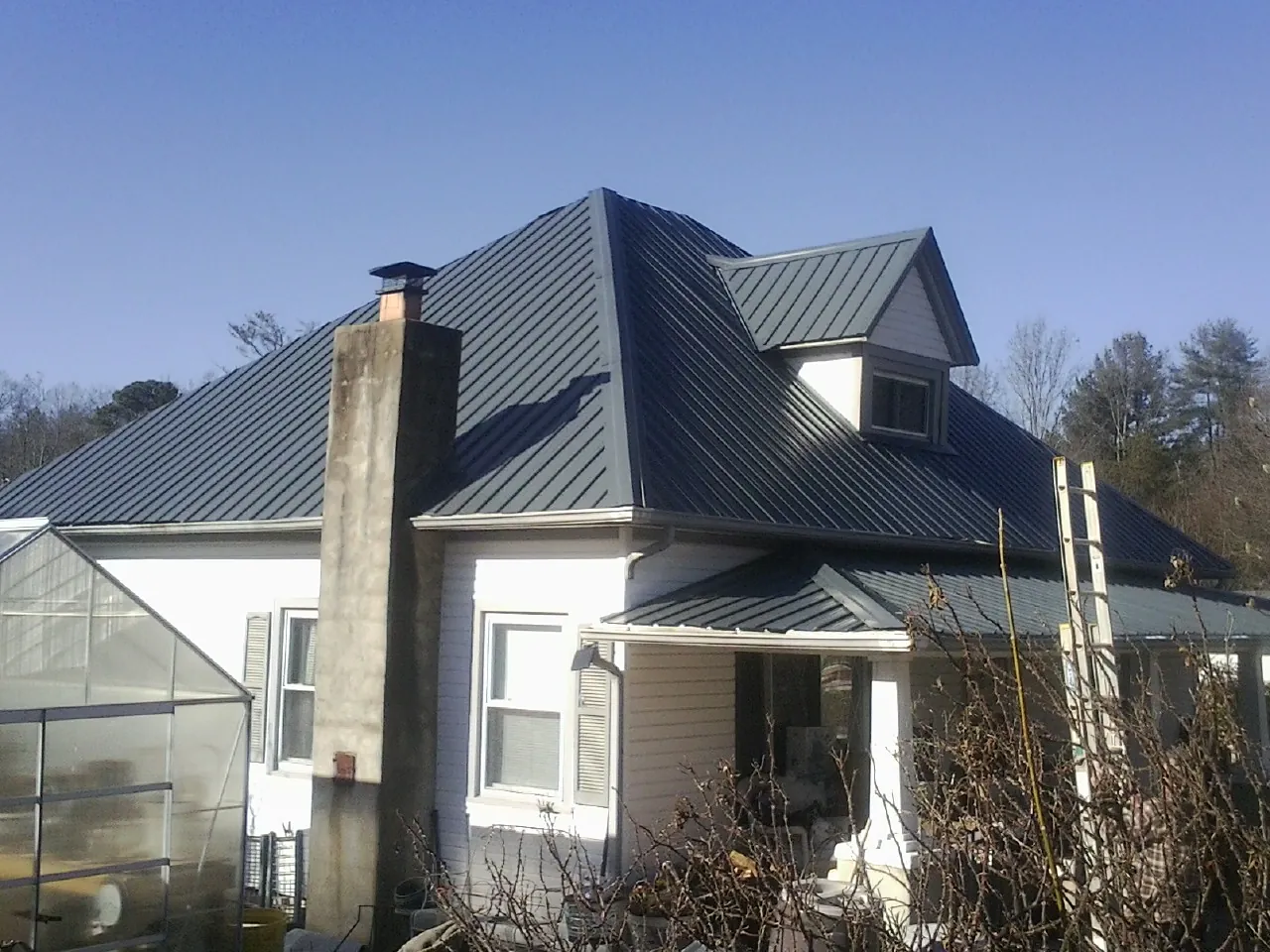 Dark blue standing seam metal roof on a white farmhouse with dormer — Slate & Tile Roof Repair by Roofing Brothers in Richlands