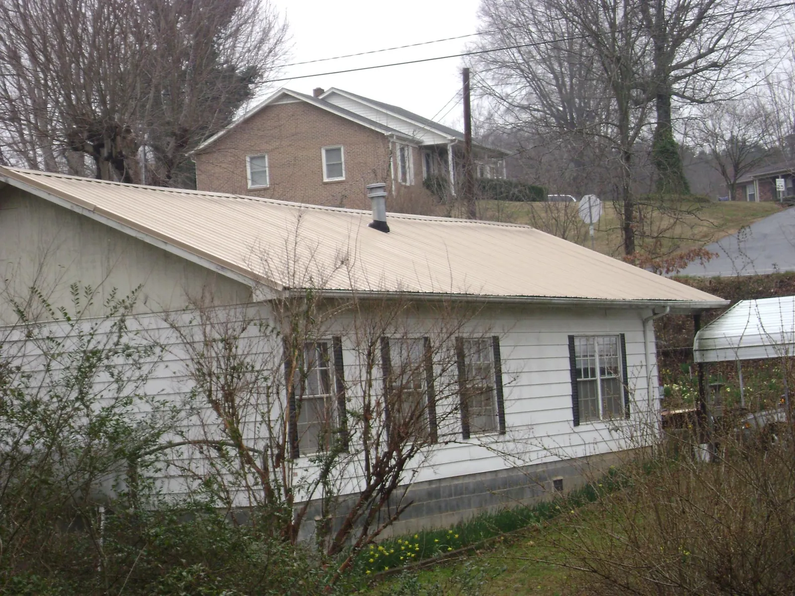 Tan metal roof on a white sided house set into a hillside — Commercial Roofing by Roofing Brothers in Richlands