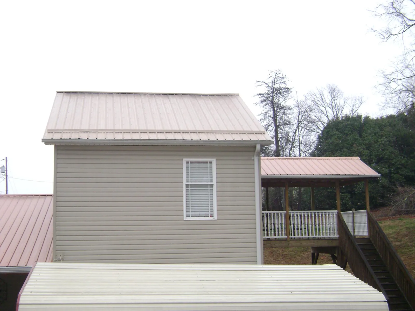 Tan metal roofs on a two story addition and attached porch, from a Roof Replacement job in Richlands